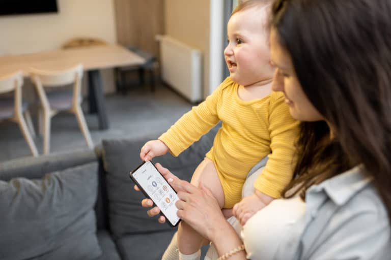 mom controlling home devices by smartphone standing with baby home